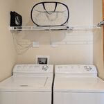 Laundry area.  Washing machine on left. Dryer on right. Shelving overhead provides more storage. Looking West.
